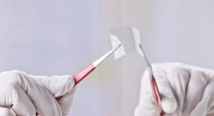 Hands of scientific showing a piece of graphene with hexagonal molecule.